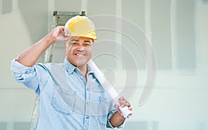 Hispanic Male Contractor with Blueprint Plans Wearing Hard Hat In Front of Drywall and Ladder