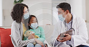 Hispanic male doctor talking to mother and daughter at home, all wearing face masks