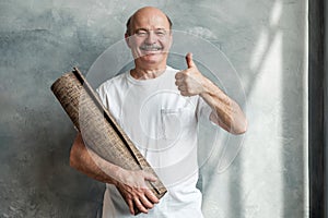 Hispanic male pensioner looking at camera while holding yoga mat in hands