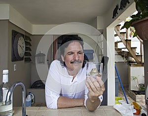 Hispanic mam looking at and holding glass of water with frog