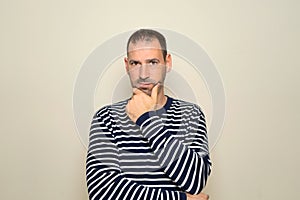 Hispanic man with beard about 40 years old wearing striped sweater thinking concentrated in doubt with finger on chin