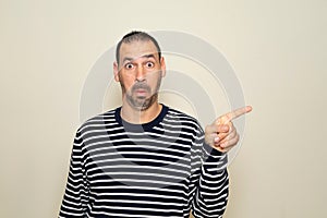 Hispanic man with beard in his 40s wearing a striped sweater pointing to the side with finger with a surprised face