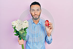 Hispanic man with beard holding bouquet of flowers and engagement ring relaxed with serious expression on face