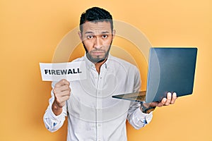 Hispanic man with beard holding computer laptop and firewall banner depressed and worry for distress, crying angry and afraid