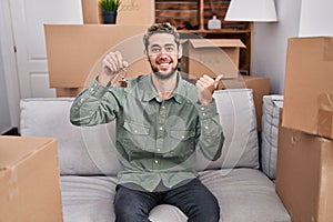 Hispanic man with beard holding keys of new home pointing thumb up to the side smiling happy with open mouth