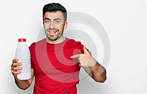 Hispanic man with beard holding liter bottle of milk pointing finger to one self smiling happy and proud