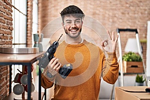 Hispanic man with beard holding screwdriver at new home doing ok sign with fingers, smiling friendly gesturing excellent symbol