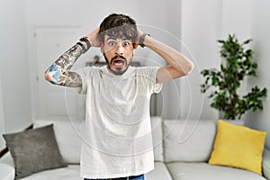 Hispanic man with beard at the living room at home crazy and scared with hands on head, afraid and surprised of shock with open