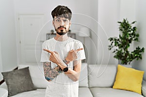 Hispanic man with beard at the living room at home pointing to both sides with fingers, different direction disagree