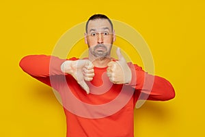 Hispanic man with beard making good and bad signs. Person undecided between yes or no on isolated yellow background.