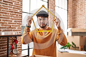 Hispanic man with beard moving to a new home holding ruler clueless and confused expression