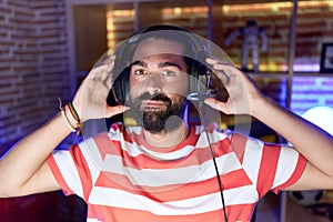 Hispanic man with beard playing video games wearing headphones relaxed with serious expression on face
