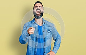 Hispanic man with beard pointing with finger to camera angry and mad screaming frustrated and furious, shouting with anger looking