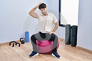 Hispanic man with beard sitting on pilate balls at yoga room confuse and wonder about question