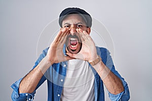 Hispanic man with beard standing over isolated background shouting angry out loud with hands over mouth