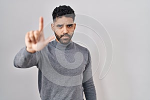 Hispanic man with beard standing over white background pointing with finger up and angry expression, showing no gesture
