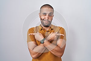 Hispanic man with beard standing over white background pointing to both sides with fingers, different direction disagree