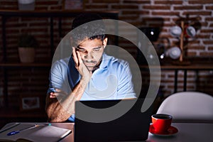 Hispanic man with beard using laptop at night thinking looking tired and bored with depression problems with crossed arms