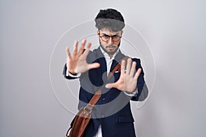 Hispanic man with beard wearing business clothes afraid and terrified with fear expression stop gesture with hands, shouting in