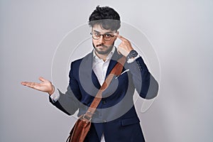 Hispanic man with beard wearing business clothes confused and annoyed with open palm showing copy space and pointing finger to