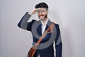Hispanic man with beard wearing business clothes very happy and smiling looking far away with hand over head