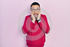 Hispanic man with beard wearing business shirt and glasses afraid and shocked, surprise and amazed expression with hands on face