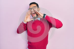 Hispanic man with beard wearing business shirt and glasses shouting angry out loud with hands over mouth