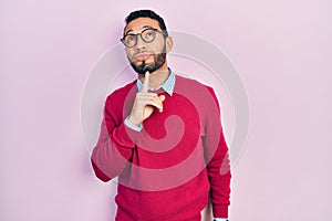 Hispanic man with beard wearing business shirt and glasses thinking concentrated about doubt with finger on chin and looking up