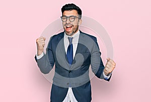 Hispanic man with beard wearing business suit and tie very happy and excited doing winner gesture with arms raised, smiling and