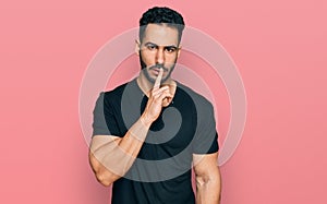 Hispanic man with beard wearing casual black t shirt asking to be quiet with finger on lips