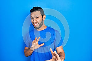 Hispanic man with beard wearing casual blue t shirt disgusted expression, displeased and fearful doing disgust face because