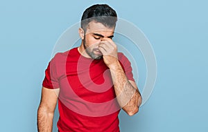 Hispanic man with beard wearing casual red t shirt tired rubbing nose and eyes feeling fatigue and headache
