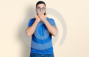 Hispanic man with beard wearing casual t shirt and glasses shocked covering mouth with hands for mistake