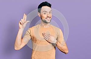 Hispanic man with beard wearing casual t shirt smiling swearing with hand on chest and fingers up, making a loyalty promise oath