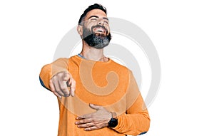 Hispanic man with beard wearing casual winter sweater laughing at you, pointing finger to the camera with hand over body, shame