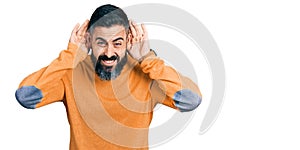 Hispanic man with beard wearing casual winter sweater trying to hear both hands on ear gesture, curious for gossip