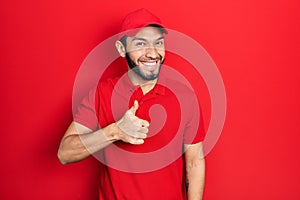 Hispanic man with beard wearing delivery uniform and cap doing happy thumbs up gesture with hand