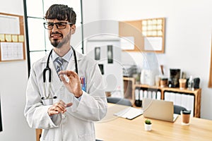 Hispanic man with beard wearing doctor uniform and stethoscope at the office disgusted expression, displeased and fearful doing