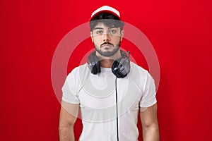 Hispanic man with beard wearing gamer hat and headphones relaxed with serious expression on face