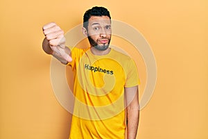 Hispanic man with beard wearing t shirt with happiness word message looking unhappy and angry showing rejection and negative with
