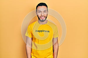 Hispanic man with beard wearing t shirt with happiness word message relaxed with serious expression on face