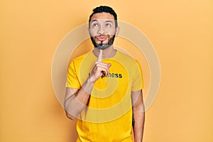 Hispanic man with beard wearing t shirt with happiness word message thinking concentrated about doubt with finger on chin and