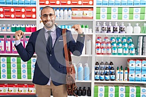 Hispanic man with beard working as salesman at pharmacy drugstore looking confident with smile on face, pointing oneself with