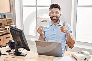 Hispanic man with beard working at the office with laptop holding thanks banner smiling happy and positive, thumb up doing