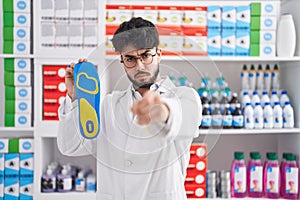 Hispanic man with beard working at pharmacy drugstore holding insole pointing with finger to the camera and to you, confident