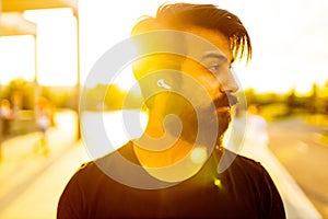 hispanic man in black cotton t-shirt listening a music with earpod in summer park outdoor golden lights