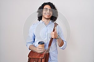Hispanic man with curly hair drinking a cup of take away coffee doing happy thumbs up gesture with hand