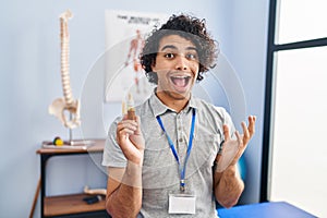 Hispanic man with curly hair holding cbd oil celebrating victory with happy smile and winner expression with raised hands