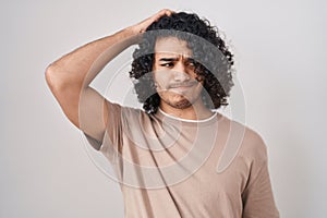 Hispanic man with curly hair standing over white background confuse and wondering about question