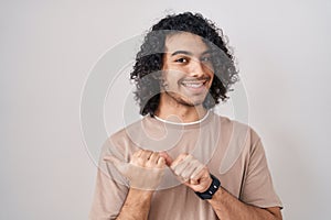 Hispanic man with curly hair standing over white background pointing to the back behind with hand and thumbs up, smiling confident